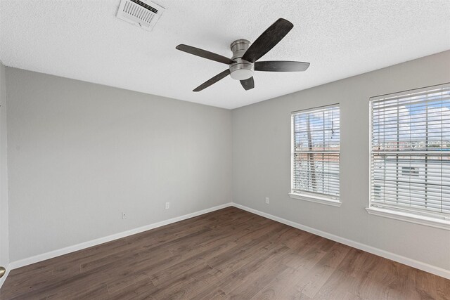 unfurnished room featuring dark wood-style floors, visible vents, a textured ceiling, and baseboards