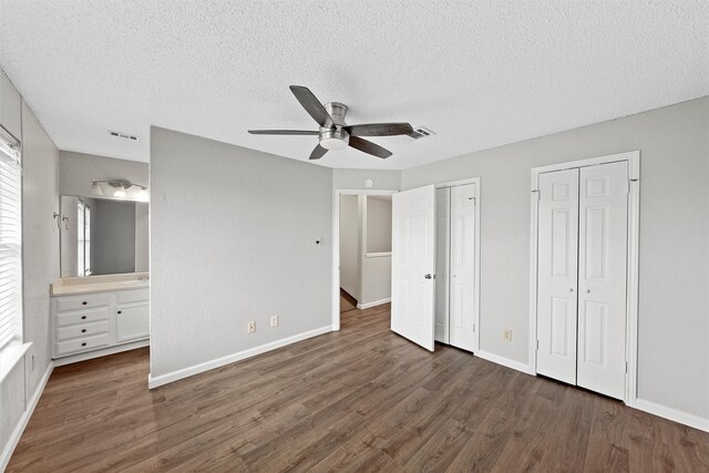 unfurnished bedroom featuring dark wood-type flooring, visible vents, and multiple closets