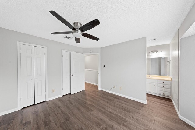 unfurnished bedroom with multiple closets, dark wood finished floors, visible vents, and baseboards