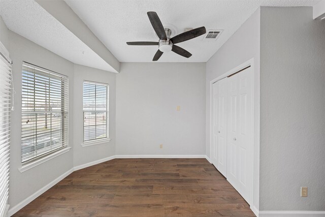 unfurnished bedroom with a textured ceiling, dark wood-style flooring, visible vents, baseboards, and a closet