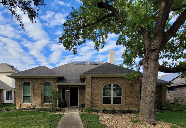 ranch-style home featuring a shingled roof, brick siding, a chimney, and a front lawn