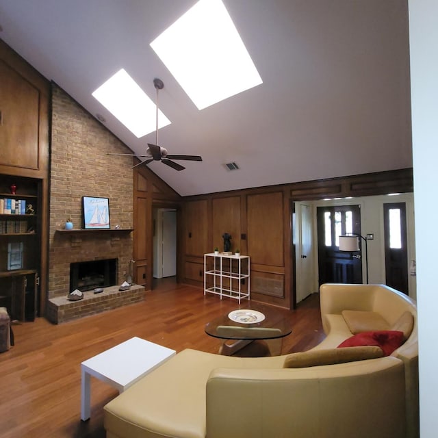 living room with lofted ceiling with skylight, a brick fireplace, visible vents, and wood finished floors