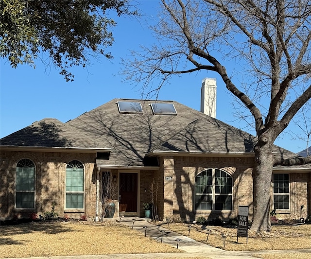 view of front of house featuring a shingled roof, brick siding, and a chimney