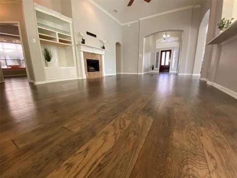 unfurnished living room featuring baseboards, dark wood finished floors, ornamental molding, a fireplace, and ceiling fan with notable chandelier