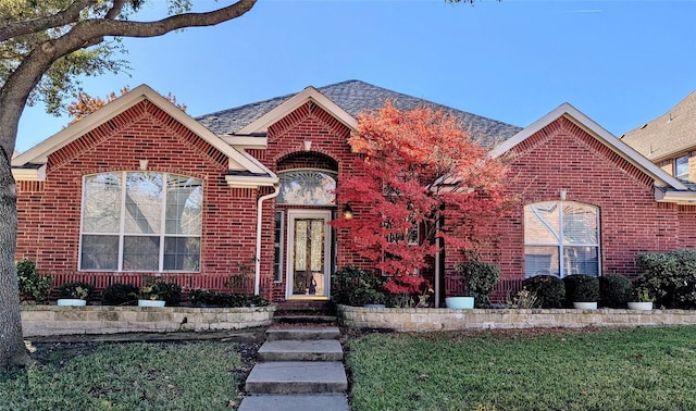 view of front of property featuring roof with shingles, a front lawn, and brick siding