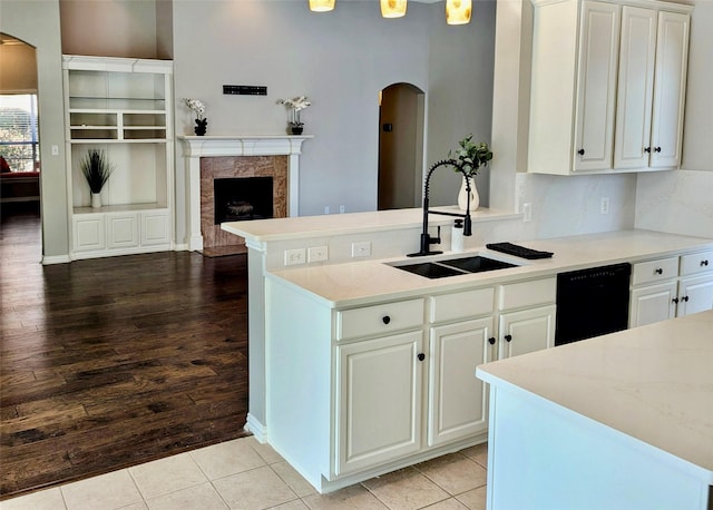 kitchen featuring black dishwasher, arched walkways, a premium fireplace, white cabinetry, and a sink