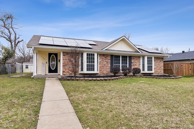 ranch-style house featuring brick siding, fence, a gate, roof mounted solar panels, and a front lawn