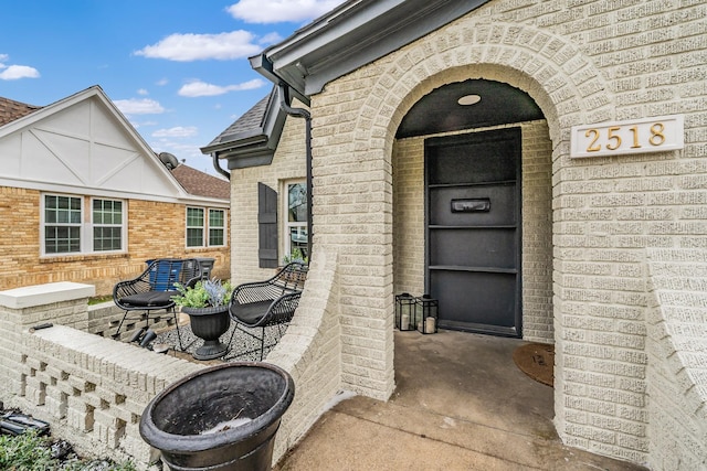 property entrance featuring a patio area, roof with shingles, and brick siding