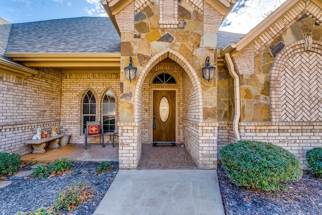 entrance to property featuring brick siding and a shingled roof