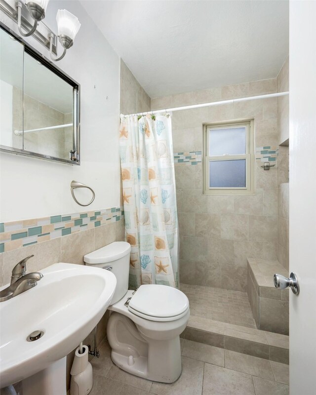 bathroom with tile patterned flooring, toilet, a sink, tile walls, and a shower stall