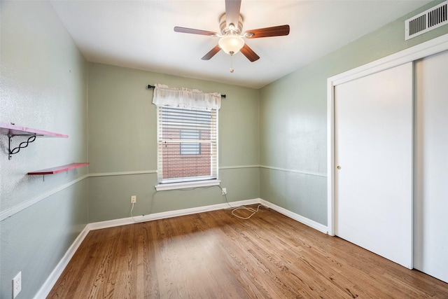 unfurnished bedroom featuring a closet, visible vents, a ceiling fan, wood finished floors, and baseboards