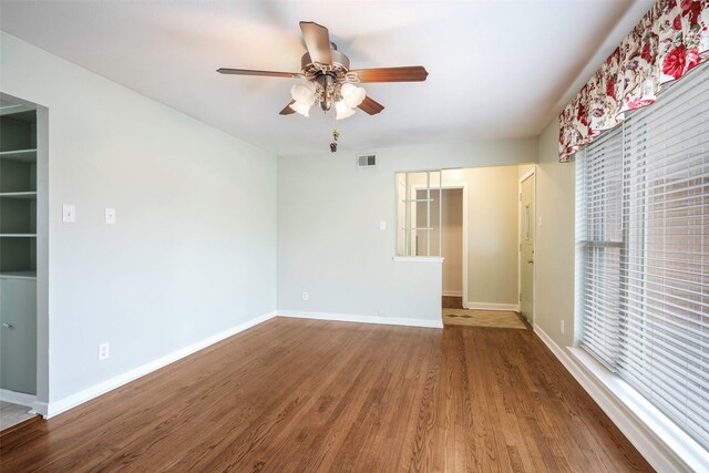 empty room with a ceiling fan, baseboards, visible vents, and wood finished floors