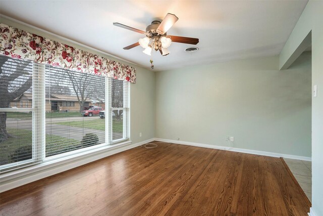 empty room with baseboards, visible vents, ceiling fan, and wood finished floors