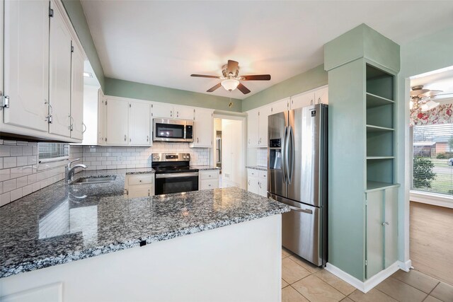 kitchen with stainless steel appliances, white cabinetry, a sink, dark stone countertops, and a peninsula