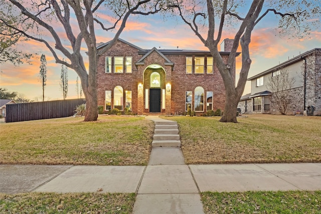 view of front of house with brick siding, fence, and a front lawn