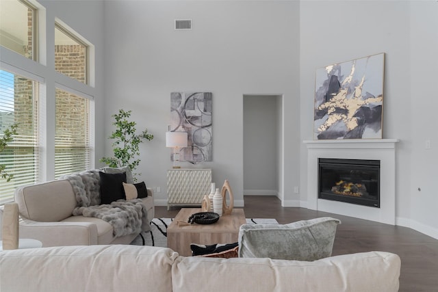 living area featuring a high ceiling, wood finished floors, visible vents, baseboards, and a glass covered fireplace