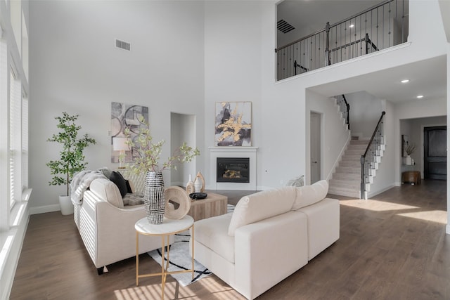 living room featuring a glass covered fireplace, wood finished floors, visible vents, and stairs