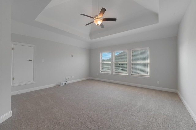 spare room with a raised ceiling, light colored carpet, and baseboards