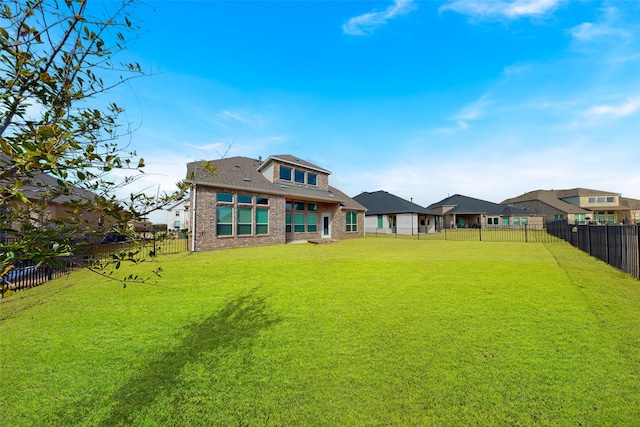 rear view of property featuring a yard, brick siding, and a fenced backyard