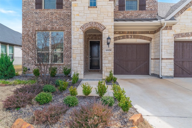 doorway to property with concrete driveway, a shingled roof, stone siding, and fence