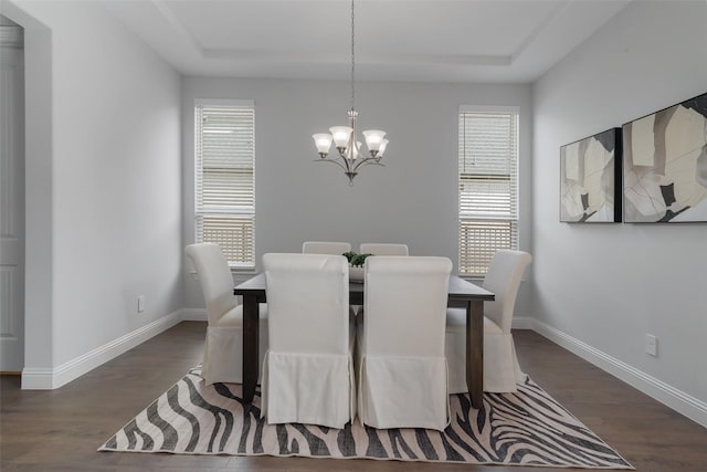 dining room with wood finished floors, plenty of natural light, a raised ceiling, and a notable chandelier