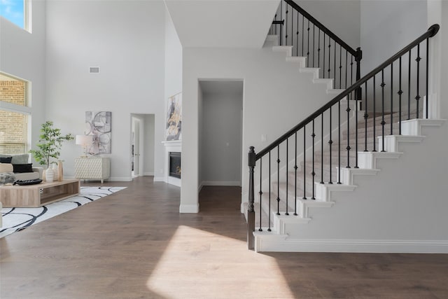 entryway featuring wood finished floors, a towering ceiling, baseboards, stairs, and a glass covered fireplace