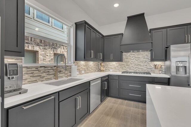 kitchen featuring tasteful backsplash, stainless steel appliances, light countertops, premium range hood, and a sink