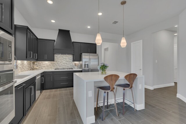 kitchen featuring dark cabinetry, light countertops, appliances with stainless steel finishes, a kitchen island, and premium range hood