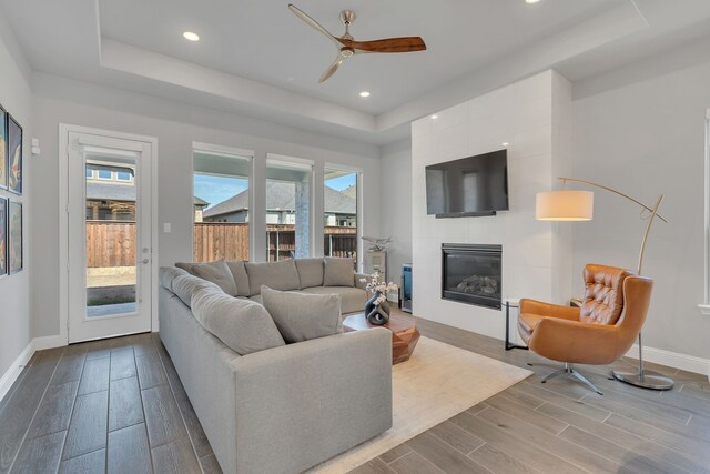 living room with baseboards, a tray ceiling, a tiled fireplace, and wood finish floors