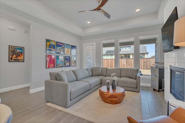 living area featuring wood finish floors, a tray ceiling, baseboards, and recessed lighting