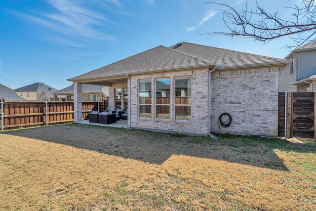 rear view of property with a shingled roof, a fenced backyard, a yard, a patio area, and brick siding