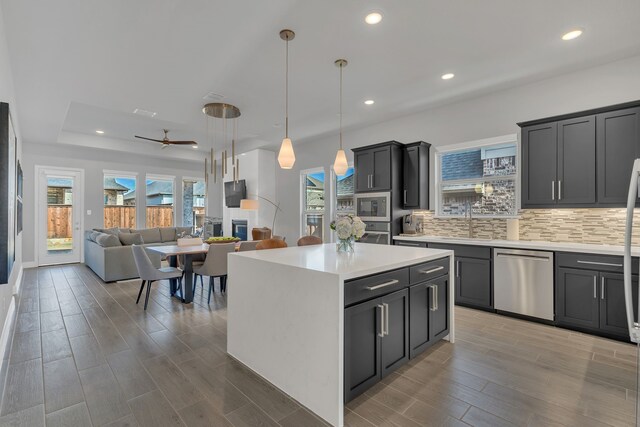 kitchen featuring stainless steel appliances, tasteful backsplash, light countertops, hanging light fixtures, and a kitchen island