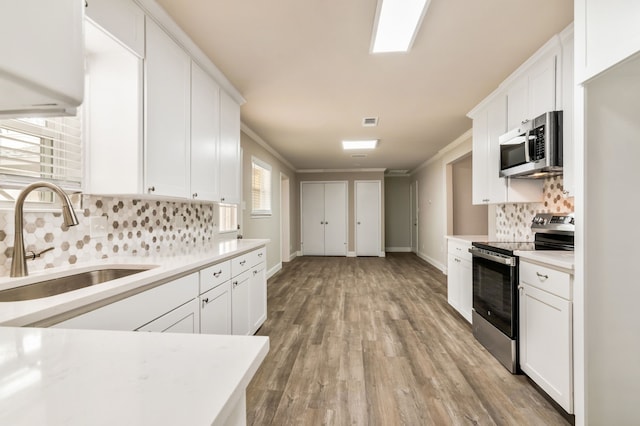 kitchen with a sink, white cabinetry, light countertops, appliances with stainless steel finishes, and backsplash