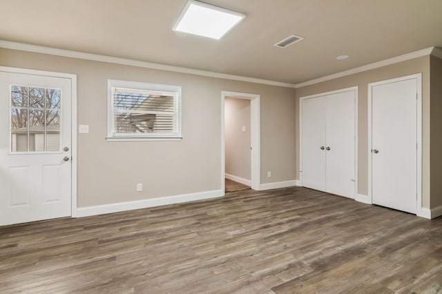 interior space featuring baseboards, wood finished floors, visible vents, and crown molding