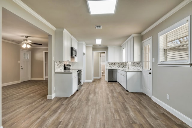 kitchen with light countertops, appliances with stainless steel finishes, light wood-style floors, ornamental molding, and white cabinetry