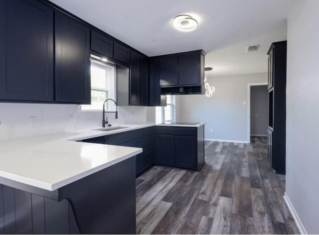 kitchen featuring dark wood-style floors, pendant lighting, light countertops, a sink, and a peninsula