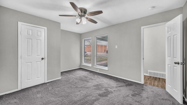 unfurnished bedroom with a ceiling fan, dark carpet, visible vents, and baseboards