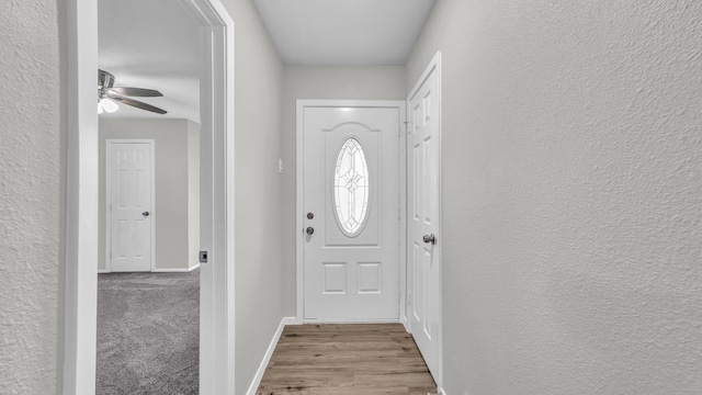 doorway with light wood-type flooring, baseboards, a ceiling fan, and a textured wall