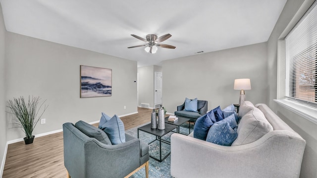 living room with a ceiling fan, visible vents, baseboards, and wood finished floors