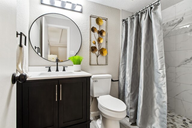 bathroom with toilet, a textured wall, tiled shower, and vanity