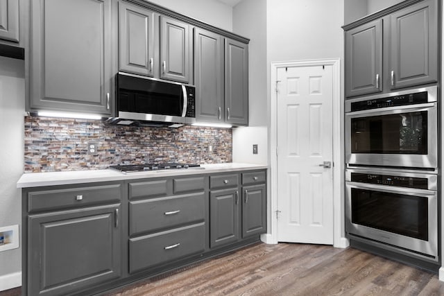 kitchen featuring dark wood finished floors, light countertops, decorative backsplash, gray cabinetry, and appliances with stainless steel finishes