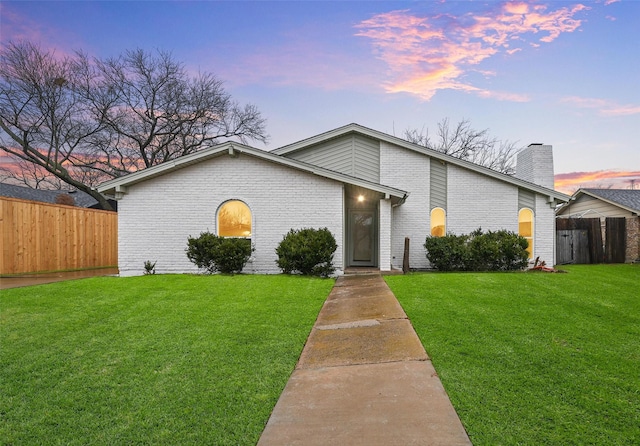 mid-century modern home with a yard, brick siding, fence, and a chimney