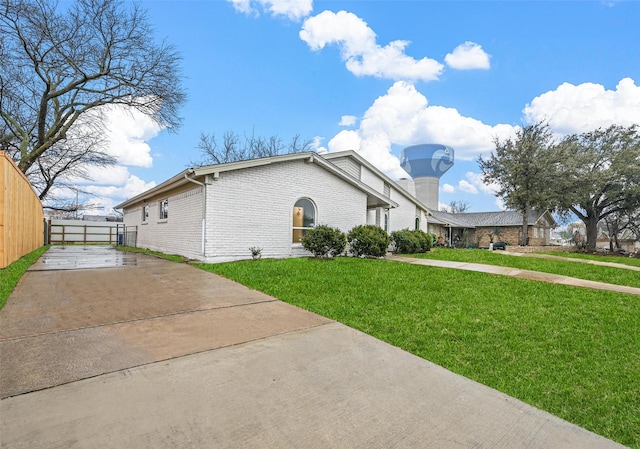 view of home's exterior featuring brick siding, fence, concrete driveway, and a yard