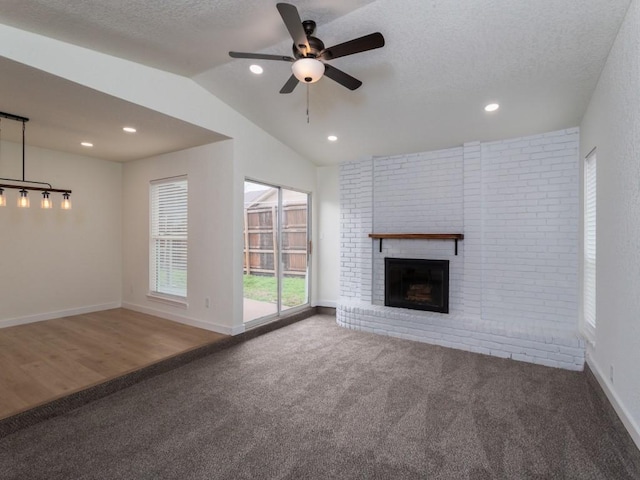 unfurnished living room with a textured ceiling, carpet flooring, baseboards, vaulted ceiling, and a brick fireplace