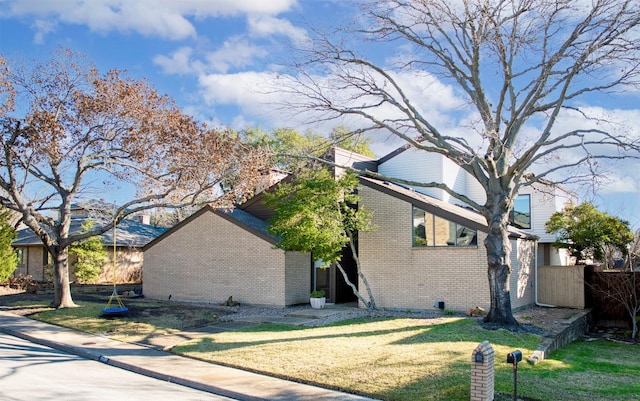 view of home's exterior with brick siding, a lawn, and fence