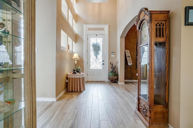 foyer featuring arched walkways, light wood-type flooring, and baseboards