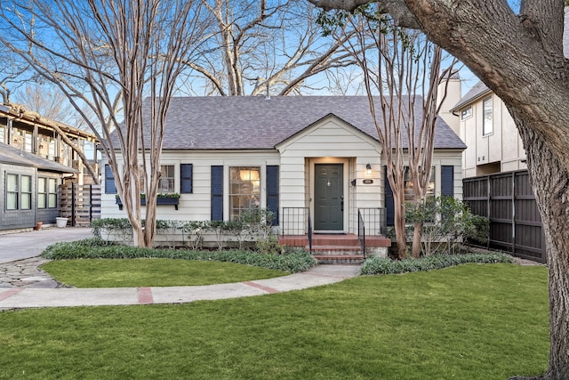 view of front of house with a shingled roof, a front yard, and fence