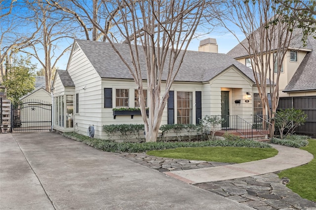 view of front of house with a shingled roof, a gate, fence, and a chimney