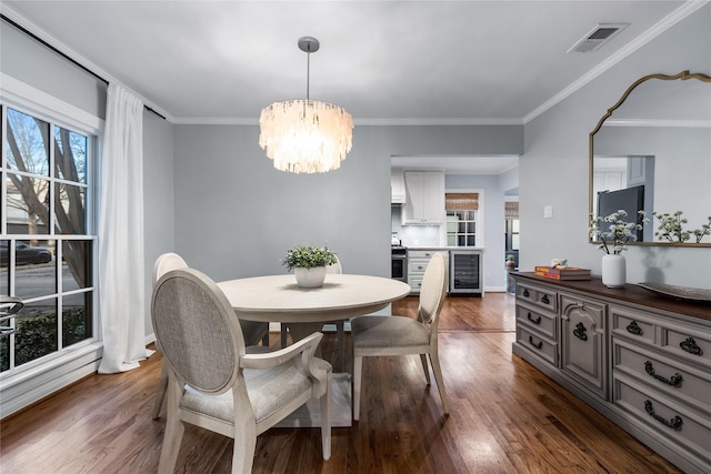 dining area with beverage cooler, visible vents, ornamental molding, dark wood finished floors, and an inviting chandelier