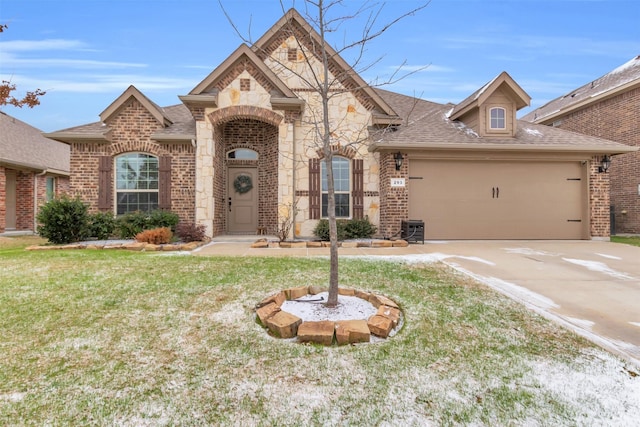 french country inspired facade with a garage, brick siding, a shingled roof, stone siding, and a front yard